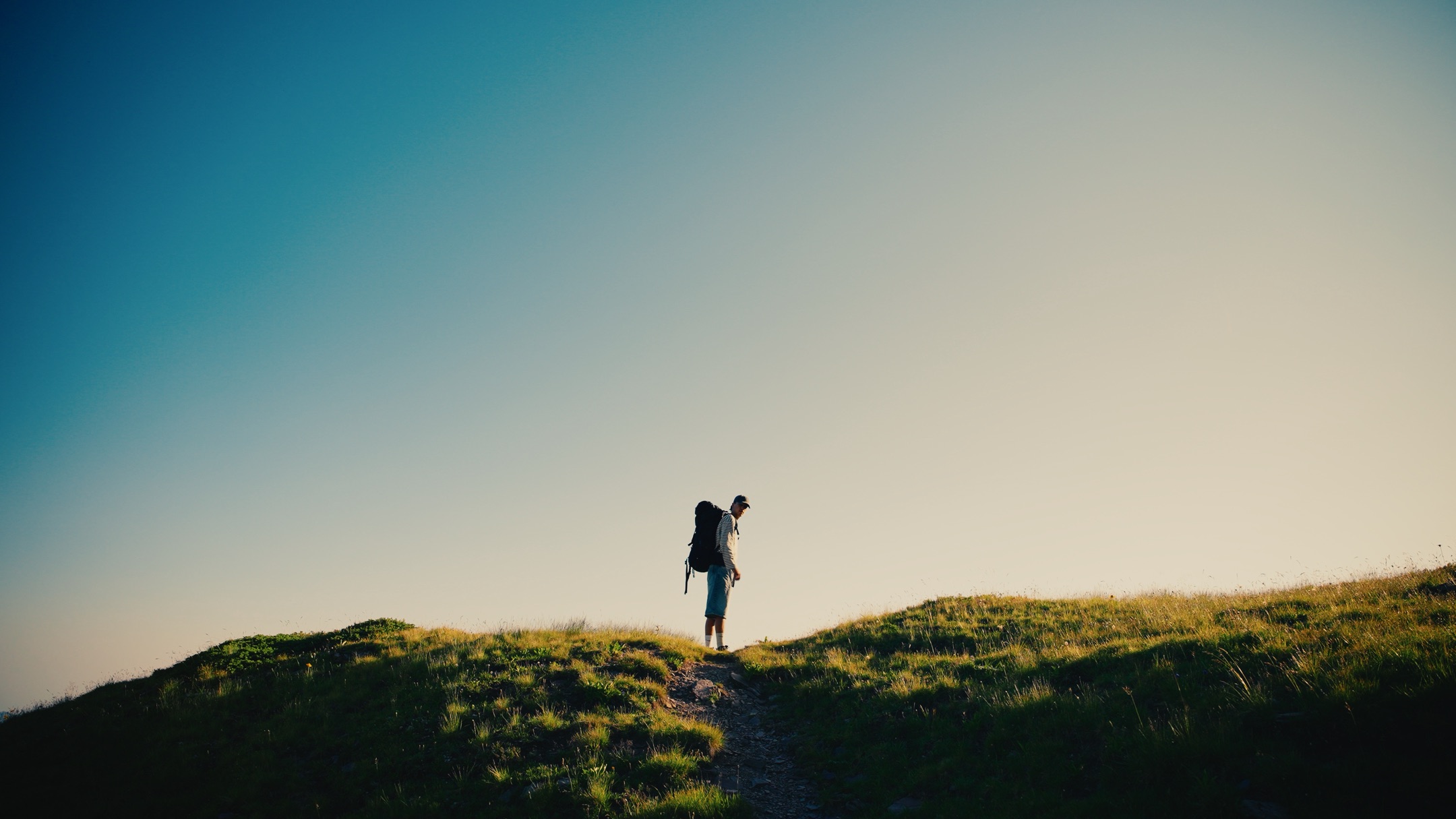 The same frame graded with the Alpine Gold LUT, lone hiker on a ridge against a deep blue sky